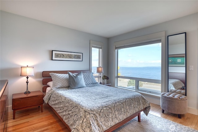 bedroom with light wood-type flooring and a water view