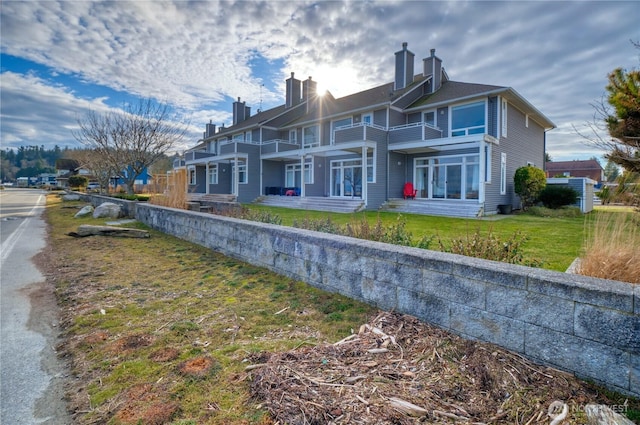 rear view of property with a lawn, a chimney, a residential view, and a balcony