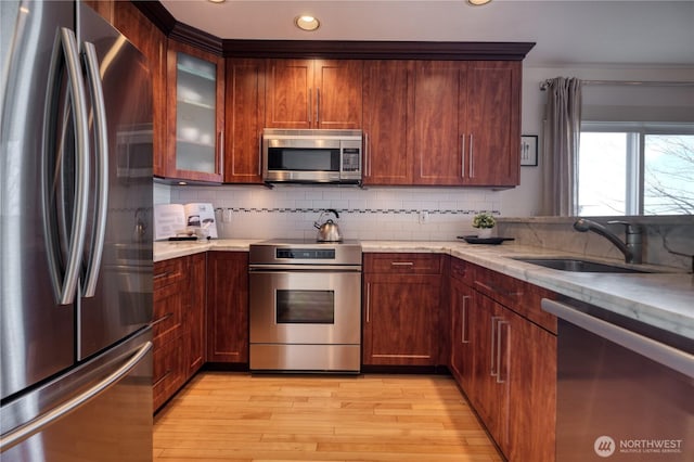 kitchen with decorative backsplash, light wood-style flooring, glass insert cabinets, stainless steel appliances, and a sink