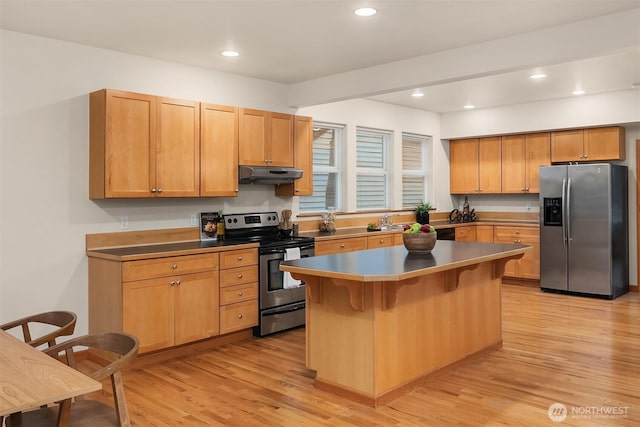 kitchen with stainless steel appliances, a breakfast bar, under cabinet range hood, and light wood finished floors