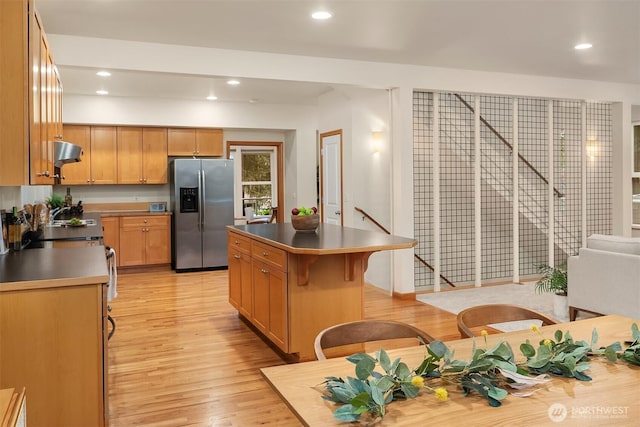 kitchen with stainless steel fridge with ice dispenser, a kitchen island, under cabinet range hood, light wood-style floors, and recessed lighting