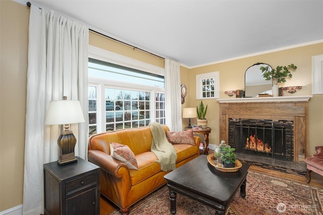 living room with crown molding, wood finished floors, baseboards, and a lit fireplace