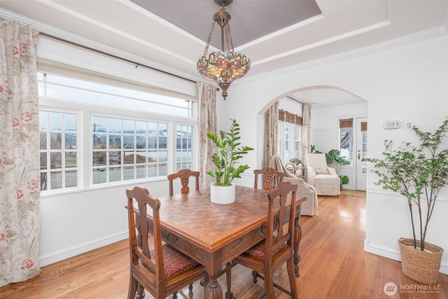 dining room with baseboards, a tray ceiling, arched walkways, crown molding, and light wood-type flooring