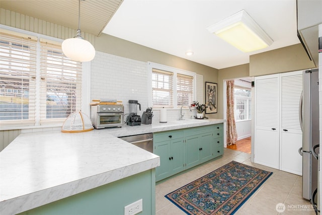 kitchen featuring green cabinets, light countertops, light tile patterned flooring, stainless steel appliances, and a sink