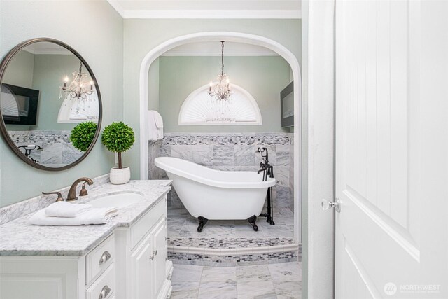 full bathroom featuring a notable chandelier, ornamental molding, vanity, and a freestanding bath