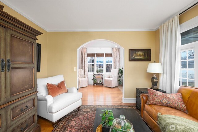 living area with arched walkways, crown molding, and wood finished floors