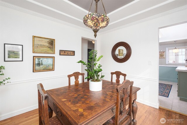 dining area with light wood finished floors, baseboards, a tray ceiling, and ornamental molding