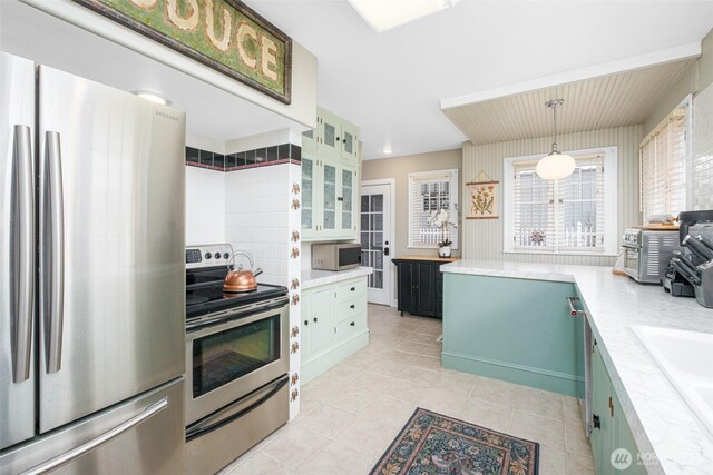 kitchen featuring light countertops, light tile patterned flooring, glass insert cabinets, and stainless steel appliances