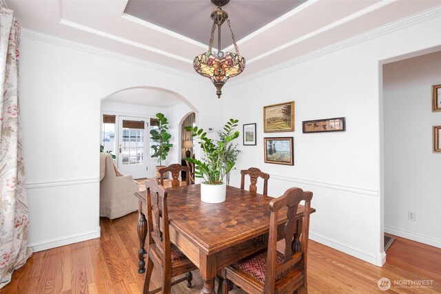 dining area featuring baseboards, a tray ceiling, arched walkways, light wood-style floors, and crown molding