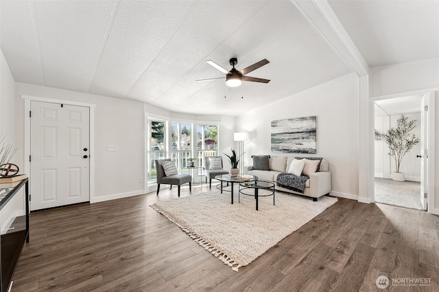 living room featuring lofted ceiling with beams, dark wood-style flooring, a ceiling fan, and baseboards