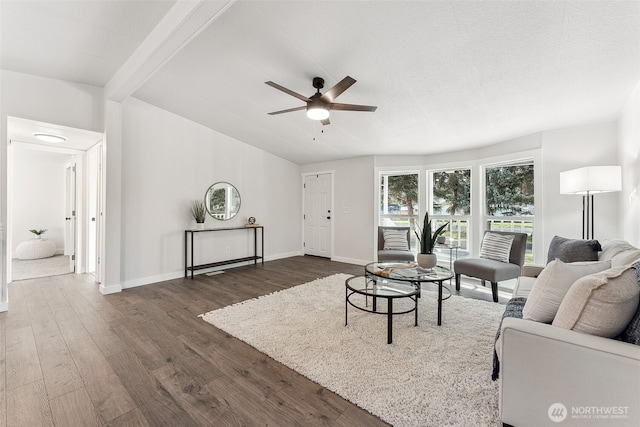 living area featuring lofted ceiling with beams, a ceiling fan, baseboards, and dark wood-type flooring