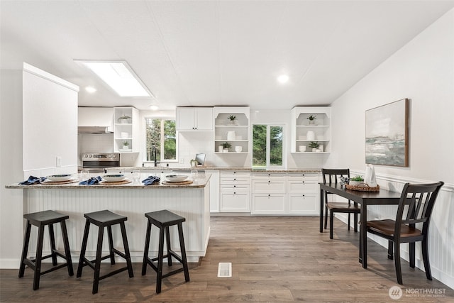 kitchen featuring stainless steel electric range oven, open shelves, wood finished floors, and white cabinets