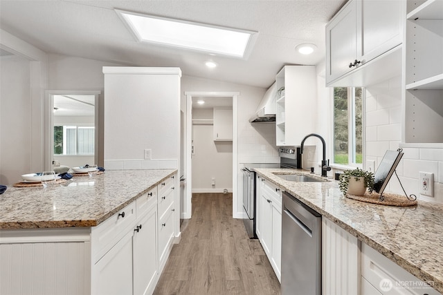 kitchen with light wood-style flooring, a sink, appliances with stainless steel finishes, tasteful backsplash, and lofted ceiling with skylight