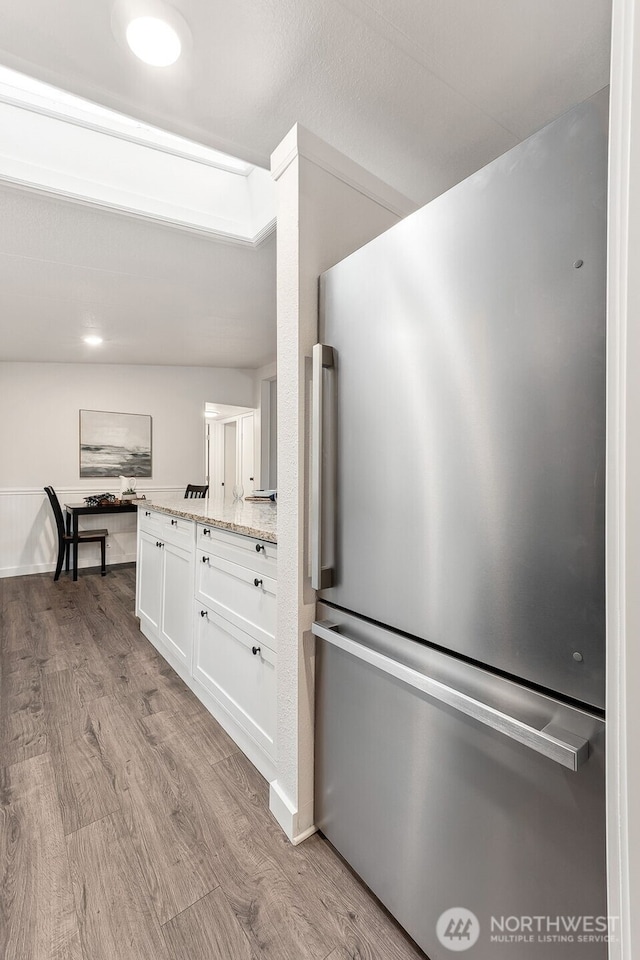 kitchen with light wood-type flooring, white cabinetry, light stone counters, and freestanding refrigerator