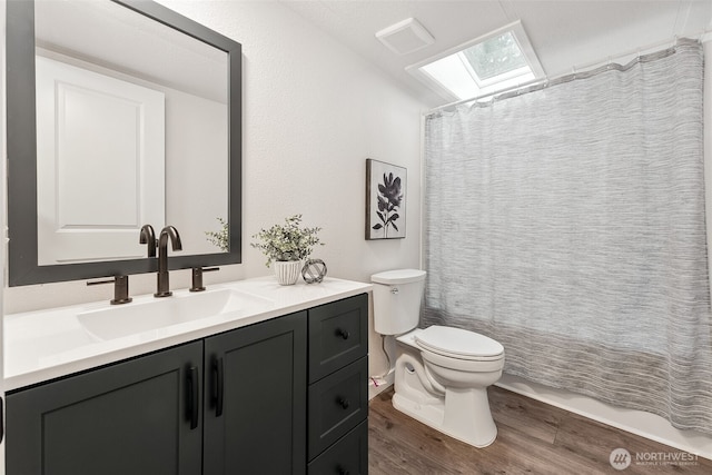 bathroom featuring a skylight, visible vents, toilet, vanity, and wood finished floors