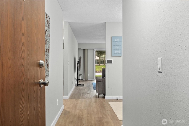 corridor featuring a textured wall, a textured ceiling, baseboards, and wood finished floors