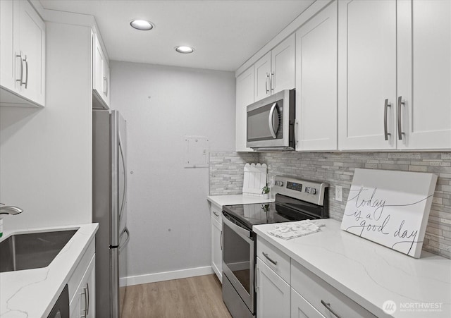 kitchen featuring decorative backsplash, appliances with stainless steel finishes, light stone countertops, white cabinetry, and a sink