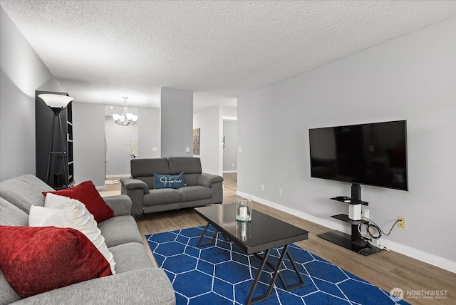 living room with a chandelier, a textured ceiling, wood finished floors, and baseboards