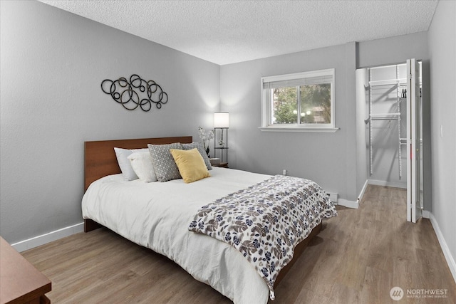 bedroom with a textured ceiling, baseboards, and wood finished floors