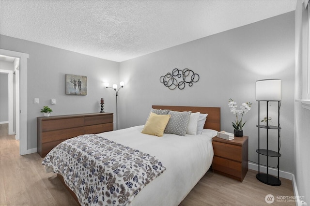 bedroom with light wood-style flooring, baseboards, and a textured ceiling