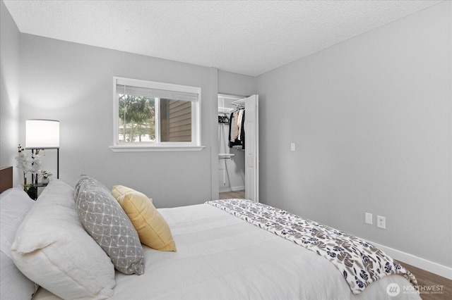 bedroom featuring a textured ceiling, wood finished floors, baseboards, a closet, and a walk in closet