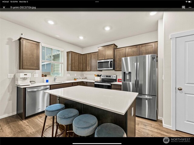 5609 151st Street Ct E, Puyallup, WA 98375 - kitchen featuring stainless steel appliances, a sink, light wood-style flooring, a breakfast bar area, and light countertops