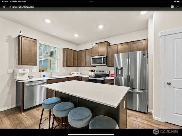 5609 151st Street Ct E, Puyallup, WA 98375 - kitchen with appliances with stainless steel finishes, a sink, light wood-style flooring, a kitchen bar, and light countertops
