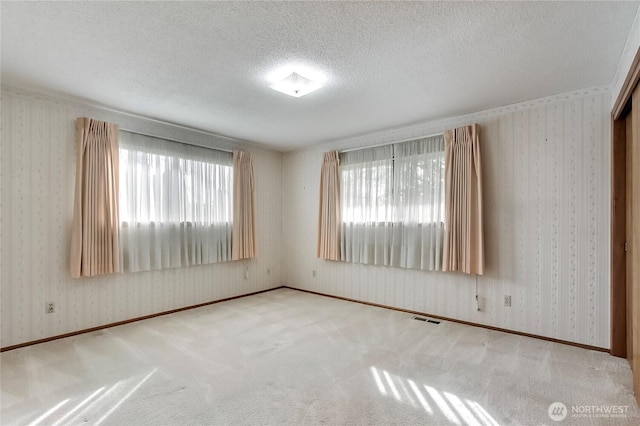 carpeted spare room with wallpapered walls, visible vents, and a textured ceiling