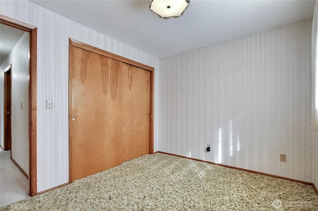 unfurnished bedroom featuring wallpapered walls, carpet flooring, and a closet