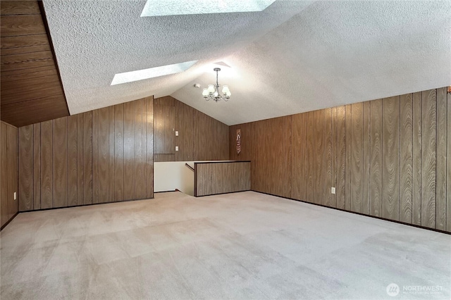 additional living space with vaulted ceiling with skylight, wooden walls, carpet flooring, and a textured ceiling