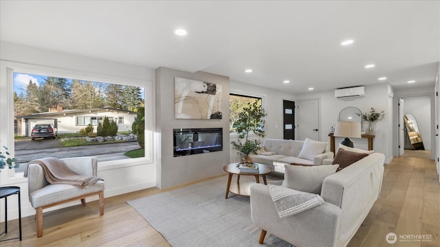 living area featuring a healthy amount of sunlight, recessed lighting, an AC wall unit, a glass covered fireplace, and light wood-type flooring