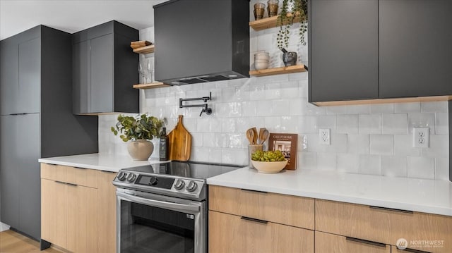 kitchen with stainless steel electric stove, light countertops, wall chimney exhaust hood, and open shelves