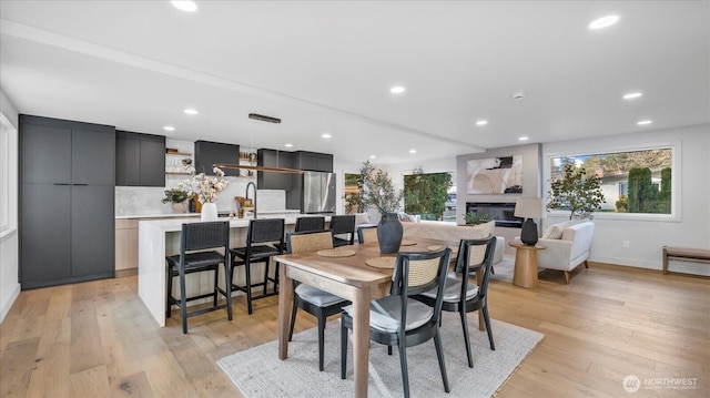 dining area featuring a glass covered fireplace, light wood-style flooring, and recessed lighting