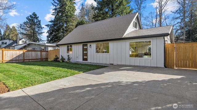 view of front of house with a patio, board and batten siding, a fenced backyard, and a front yard