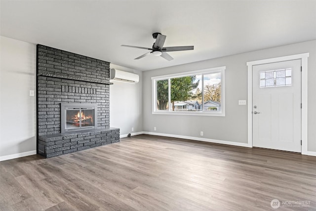 unfurnished living room featuring baseboards, a brick fireplace, an AC wall unit, and wood finished floors