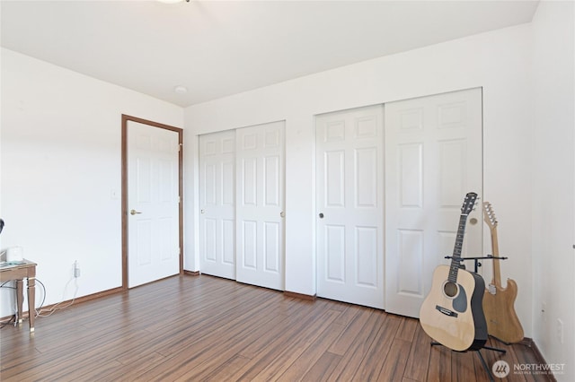 unfurnished bedroom with baseboards, two closets, and wood finished floors