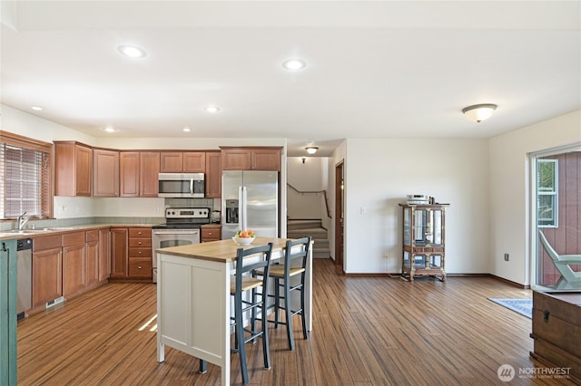 kitchen with stainless steel appliances, recessed lighting, a sink, wood finished floors, and baseboards