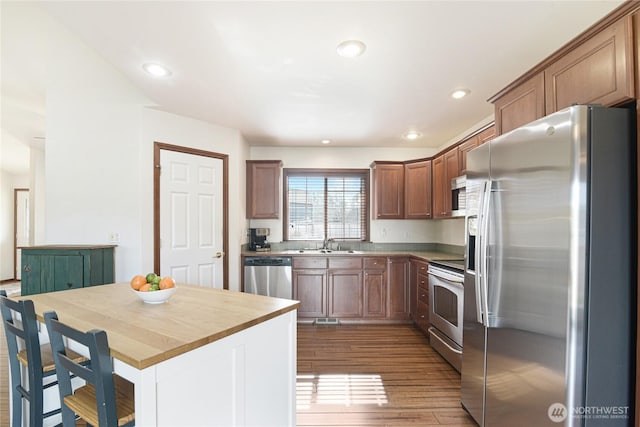 kitchen with brown cabinets, stainless steel appliances, recessed lighting, a sink, and wood finished floors