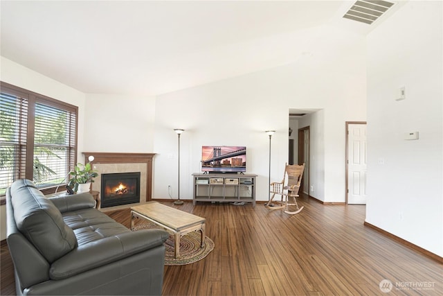 living area featuring a tile fireplace, visible vents, baseboards, and wood finished floors