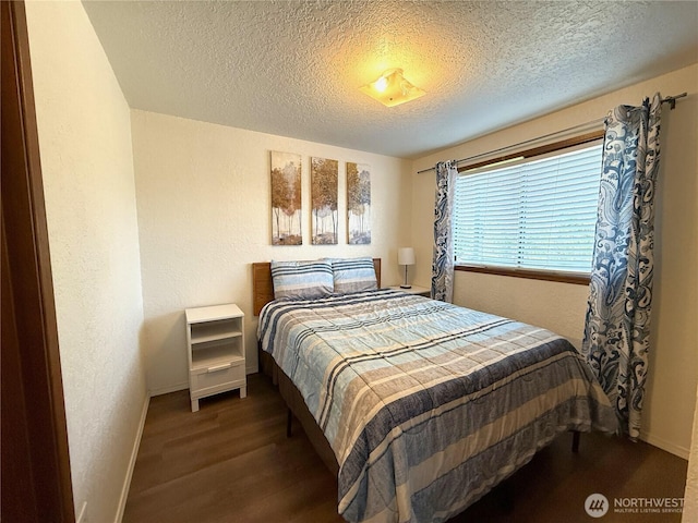 bedroom featuring a textured ceiling, a textured wall, wood finished floors, and baseboards