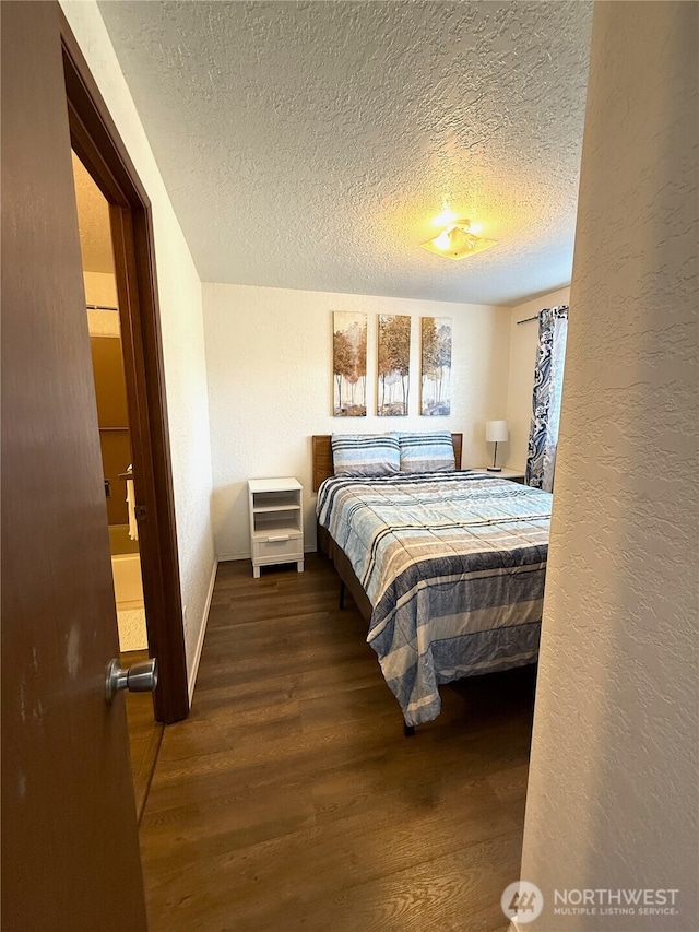 bedroom with a textured ceiling, a textured wall, wood finished floors, and baseboards