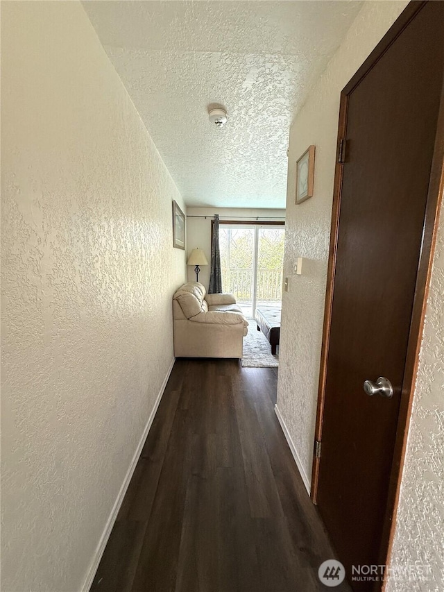 hallway with baseboards, dark wood finished floors, a textured ceiling, and a textured wall