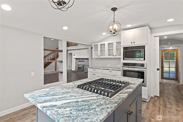 kitchen featuring glass insert cabinets, light stone countertops, light wood-style floors, white cabinets, and stainless steel appliances