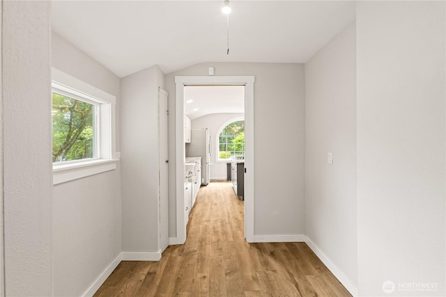 corridor featuring vaulted ceiling, light wood-style floors, and baseboards