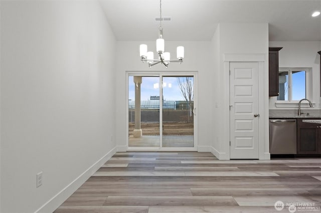 unfurnished dining area with a sink, visible vents, baseboards, light wood finished floors, and an inviting chandelier