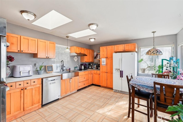 kitchen featuring decorative light fixtures, dishwasher, light countertops, white fridge with ice dispenser, and a sink