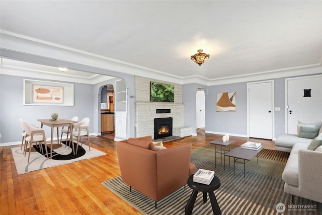 living area featuring arched walkways, crown molding, a large fireplace, wood finished floors, and baseboards