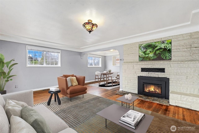 living room featuring a stone fireplace, baseboards, and wood finished floors