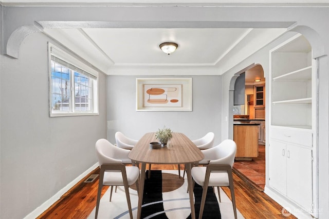 dining room with arched walkways, dark wood finished floors, visible vents, and baseboards