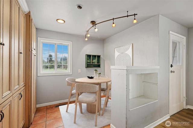 dining space featuring light tile patterned flooring, rail lighting, and baseboards